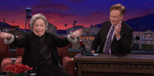 TV gif. On the Tonight Show with Conan O'Brien guest Kathy Bates eggs the audience on to boo with her as Conan sits at his desk hesitating to speak.
