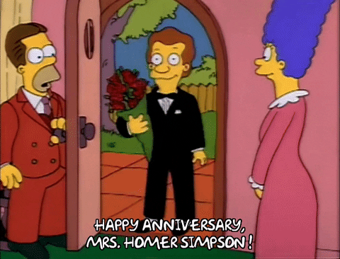 The Simpsons gif. Homer (with hair) wears a brown suit as he holds the back door open. Marge stands nearby in her nightgown, pleasantly surprised, as a man in a tuxedo holding a bouquet enters to exclaim: Text, "Happy anniversary, Mrs. Homer Simpson!"