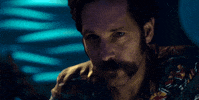 Movie gif. Paul Rudd as Cactus Bill in Mute looks at us straight and raises his glass to cheers.