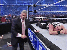 Sports gif. Vince McMahon stands next to a wrestling ring as a referee lays on the ring floor, holding onto the ropes. Suddenly a man in a suit rushes up and slams Vince into the ground, punching his forehead several times. The man gets off of Vince, leaving him on the ground, and walks away. It is then revealed that the man walking away is Donald Trump.