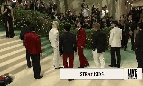 Met Gala 2024 gif. All 8 members of the K-pop band Stray Kids line up in a staggered position wearing Tommy Hilfiger three-piece suits in alternating white, navy blue, and cardinal red, all accented with the other featured colors.