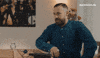 Reality TV gif. Bearded man from Eurovision taps his fingers on a table, exhales impatiently, and shifts in his seat impatiently.