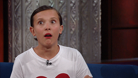 Late night gif. Millie Bobby Brown on The Late Show with Stephen Colbert sits on a couch and looks out at the crowd with large, fearful eyes. She clutches the sides of her head with her hands as tries to think.