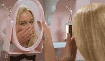 Movie gif. Christine Taylor as Marcia in "The Brady Bunch" holds up a pink plastic framed mirror and admires herself, patting her face and tousling her hair and blowing a kiss.