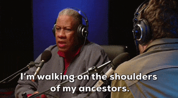 Celebrity gif. Andre Leon Talley sits for a radio interview, speaking sincerely into the microphone. Subtitle text reads, "I'm sitting on the shoulders of my ancestors.