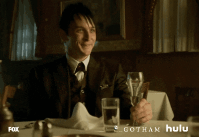 TV gif. Robin Lord Taylor as Oswald Cobblepot in Gotham smiles and raises his glass to cheers.