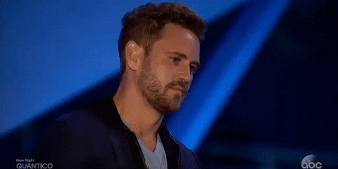 Reality TV gif. Nick Viall in The Bachelor has a neutral expression but then chuckles at something and smiles.