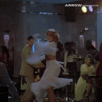 Video gif. 80s-era clip of a woman wearing a white two-piece dress with a flowing skirt and sleeves whirls and twirls around a nightclub.