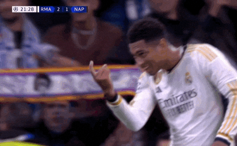 Sports gif. Jude Bellingham of Real Madrid walks across the field with a big smile on his face gesturing with his finger like he wants you to come closer.