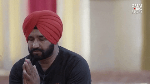 Video gif. Bearded man wearing a red turban bows his head while praying, with his hands pressed together.