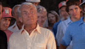 Movie gif. Ted Knight as Judge Smails in Caddyshack stands in front of a crowd of people. His eyes are wide and he shakes his head sarcastically as he says, “Well? We’re waiting!”