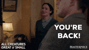 TV gif. Anna Madeley as Mrs. Hall on All Creatures Great and Small walks up to a man with a big, warm smile on her face. She says, “You're back!” and gives him a big hug.