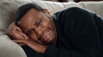 TV gif. Anthony Anderson as Dre on Blackish weeps while lying sideways on a sofa with his hands tucked under his head.