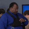 The Office gif. Leslie David Baker as Stanley stands boredly in a room full of people. He has a triangular pouch strapped to his chest. He unzips it and unapologetically takes out a slice of pizza out of the pouch. He then goes in for a big bite.