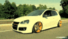Video gif. A white Volkswagen GTI with bright yellow rims drives down a road lined with lush, green trees. The driver's side window is rolled down.