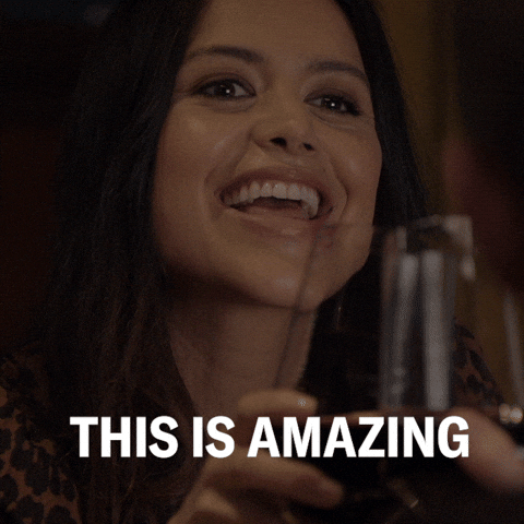 TV gif. Alyssa Diaz as Angela Lopez on The Rookie clings her wine glasses with another to toast. She has a big smile on her face as she says, “This is amazing.” Then, she sips her wine. 