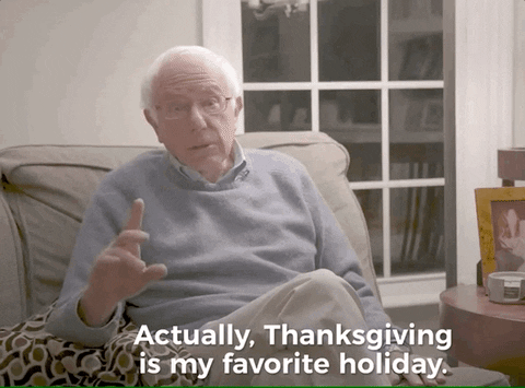 Political gif. Bernie Sanders wears a cozy, light blue sweater while sitting on the sofa. His face is very serious as he says, "Actually, Thanksgiving is my favorite holiday," which appears as text.