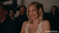 TV gif. Among an audience, on the show Nobodies, Leslie Bibb as Sam snickers quietly, raising her hand to cover her mouth.