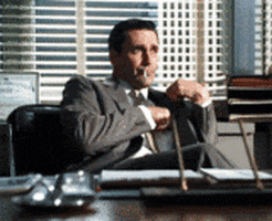 TV gif. Character Don Draper of Mad Men pulls his cigarette lighter out of his jacket, shrugs, and gestures as if to say "Whatever."