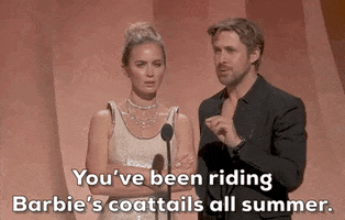 Oscars 2024 gif. Ryan Gosling whispers into the microphone, "You've been riding Barbie's coattails all summer." With her arms crossed, Emily Blunt looks completely unamused, as she rolls her eyes exasperatedly. 