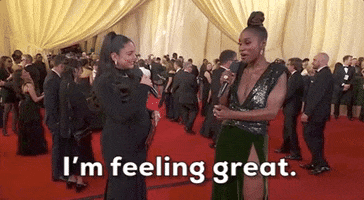 Oscars 2024 GIF. A newly pregnant Vanessa Hudgens is interviewing Issa Rae. Rae holds her microphone in one hand and gestures with her other hand, smiling and saying, "I'm feeling great!" and Hudgens laughs in response. 