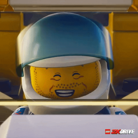 Video game gif. Closeup of a LEGO character in "LEGO 2K Drive" seated in the driver's seat of a car with his helmet on. He holds one hand up and head bangs like he's happily singing his heart out. 
