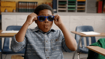 TV gif. Sitting in an empty classroom and wearing blue-rimmed sunglasses, DeVion Harris as Tyler Duda from Legendary Dudas throws his hands from his head to make the "mind blown" gesture.