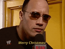 TV gif. The Rock on WWE wears sunglasses and speaks vigorously into the microphone as he looks at us and says, "Merry Christmas!"