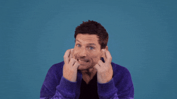 Celebrity gif. Simon Rex forces a smile as he holds up crossed fingers.