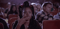 Movie gif. Regina Hall as Brenda in "Shakespeare in Blood" in a movie theater, engrossed in a movie while snacking and licking each of her fingers.
