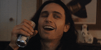 Movie gif. James Franco as Tommy in The Disaster Artist laughs as he holds up an energy drink. 
