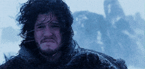 TV gif. Kit Harington as Jon in Game of Thrones, wearing full winter gear, grimaces as wind and snow pummels him in an icy landscape.