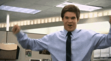 TV gif. Adam Devine as Adam Demamp on Workaholics stands in an office cubicle. He lifts his fists up in celebration and smiles excitedly.