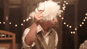 Music video gif. From Radical Face's video for "We're On Our Way," a boy wearing a poofy, curly white wig raises a wine glass and looks around.