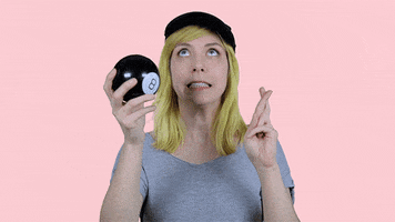 Video gif. A woman in a baseball cap shakes a Magic 8 ball and crosses her fingers, then looks to see what it says. Her eyes grow big in surprise.