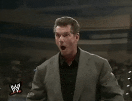 TV gif. Vince McMahon, dressed in a suit jacket, steps backward in WWE ring with a look of shock on his face, eyes and mouth wide open.