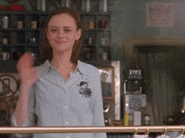 TV gif. Alexis Bledel as Rory in Gilmore Girls waves toward us with a taut smile.