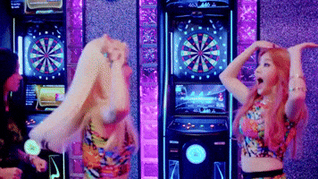 Music video gif. Min Ah and So Jin from Girl's Day in their music video for Ring My Bell. The two leap up and down in excitement and high five in front of darts boards.