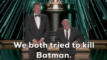 Oscars 2024 gif. Arnold Schwarzenegger towers over Danny Devito, who stands next to him. Schwarzenegger says, "We both tried to kill Batman." Devito nods in agreement. 