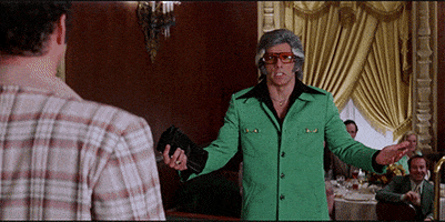 Movie gif. Ben Stiller as David in Starsky and Hutch, disguised as a man with thick gray hair, mutton chops, yellow sunglasses, and a green leisure suit, cocks his head to one side and spreads his arms confrontationally. He speaks to a man in the foreground. Text, "Do it," (repeated 3 times).