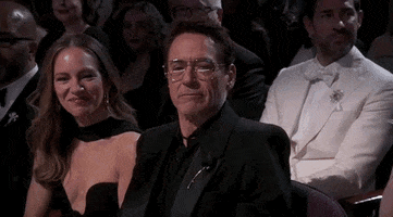 Oscars 2024 GIF. Robert Downey Junior, seated at the Oscars, pounds his heart with appreciation, then emphatically pointing at us and saying, “Thank you.”