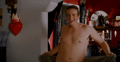 Movie gif. Jason Segal as Peter in Forgetting Sarah Marshall, naked and smiling while wiggle-dancing with a towel.