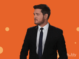 Video gif. Michael Buble catches an orange Bubly sparkling water can. He raises his eyebrows while below him flashes text reading “yum.”