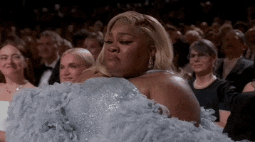 Oscars 2024 GIF. Da’Vine Joy Randolph, seated at the Oscars, uses one hand to regal cover her face and dab her eyes, overcome with emotion.