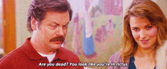 Parks and Recreation gif. Nick Offerman as Ron squints with suspicion while speaking, while Lucy Lawless as Diane looks on with a subtle smile. Text, "Are you dead? You look like you're in rictus."