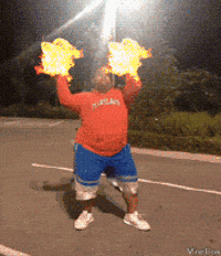 Video gif. In a parking lot at night, a young man in an orange hoodie and blue shorts performs a dance. Special effects turn the dance into a parody of Avatar: The Last Airbender with fireballs resembling cheerleading pom-poms, spinning movements creating gusts of wind, a sudden wave of water, and stone blocks rising from the ground.